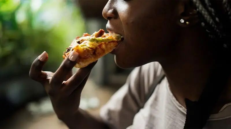 young Black person eating a slice of pizza