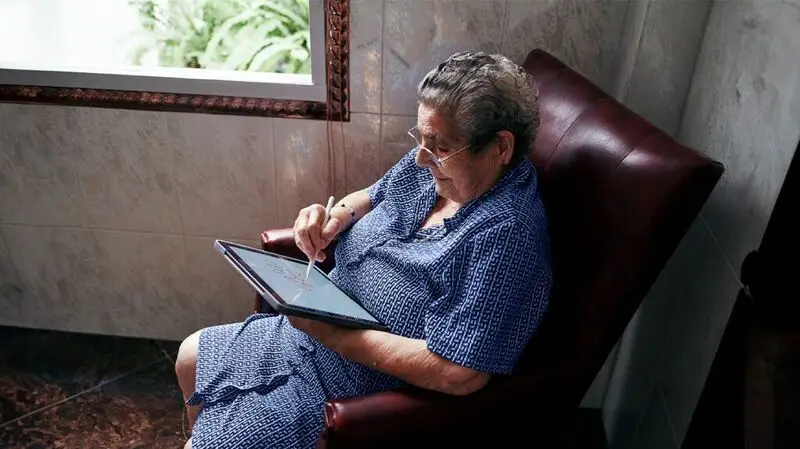 older white woman in an armchair drawing on a tablet