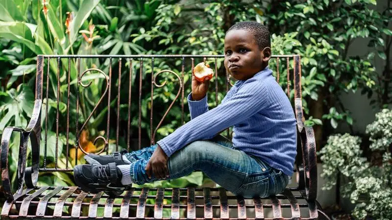 young Black child sitting on a bench eating an apple