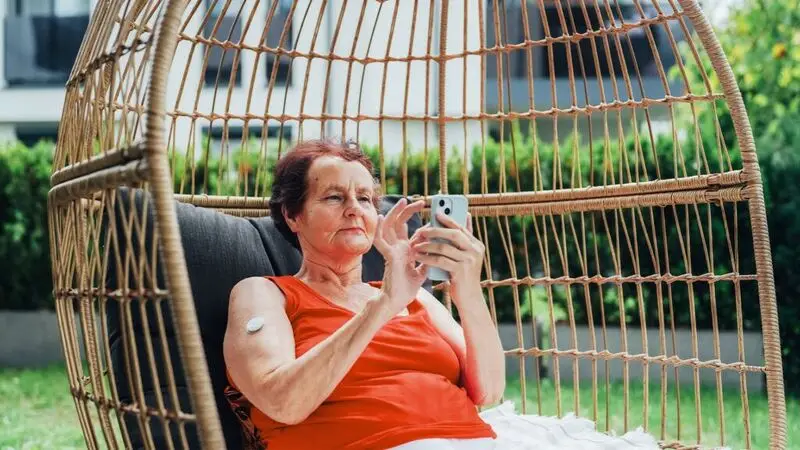 older woman sitting in wicker chair scrolling on her phone