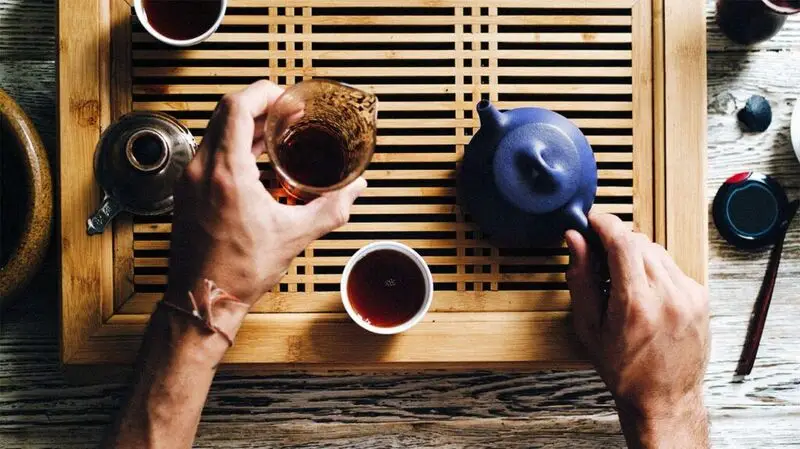 A person preparing a glass of tea with a teapot in hand