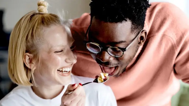 young white woman feeding a spoonful of fruit bites to a young Black man