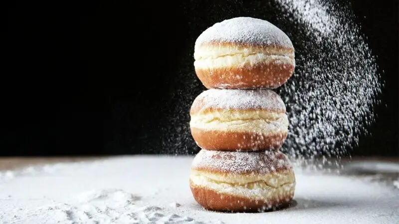 Three sugary powdered doughnuts piled on top of each other like a tower