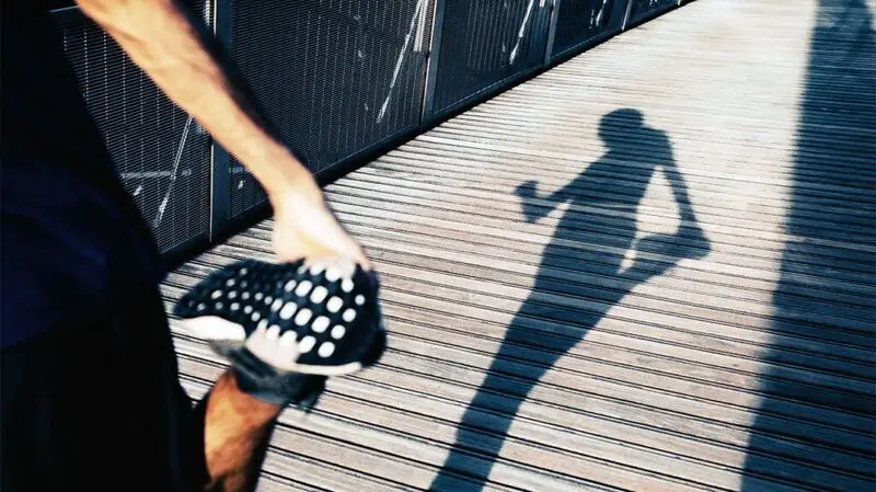 The shadow of a runner doing a standing quad stretch and looking at their smart watch