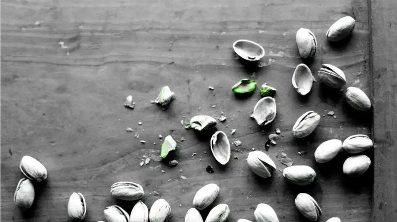 Fresh pistachios and their broken shells on a flat woody surface