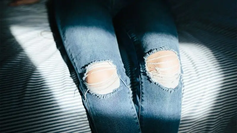 A close up of a person's knees showing through ripped jeans