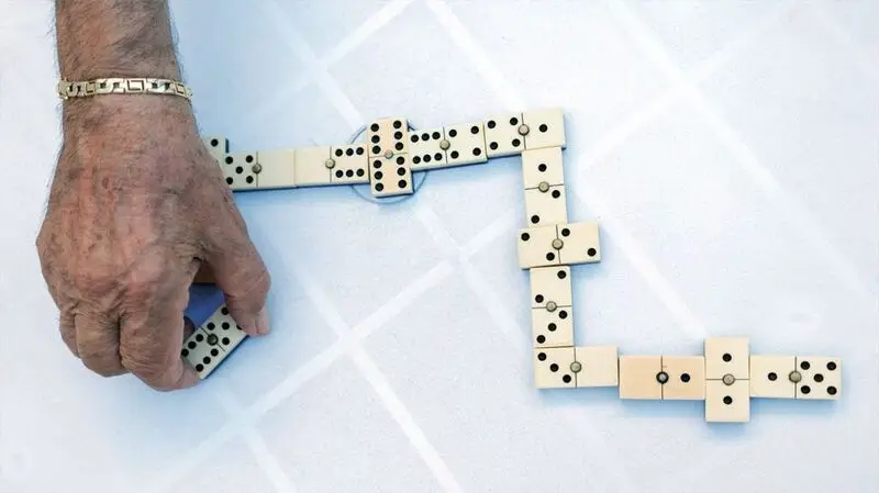 An older adult playing a game of dominos on a flat surface