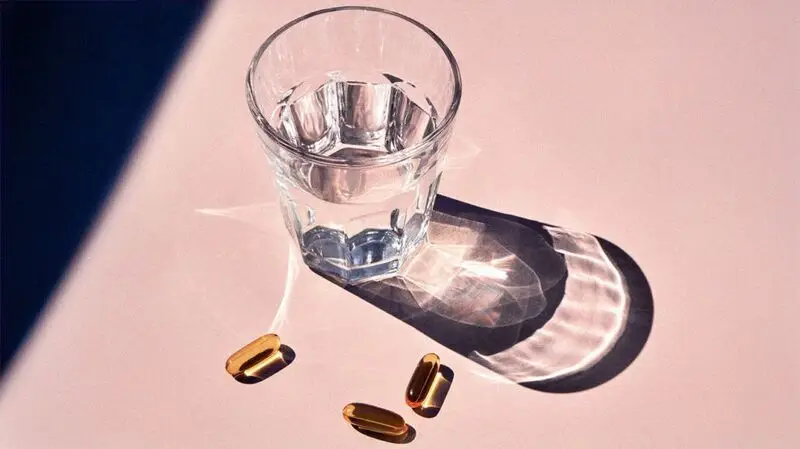 A glass of water and 3 capsules of fish oil, rich in omega-3 and omega-6 fatty acids.