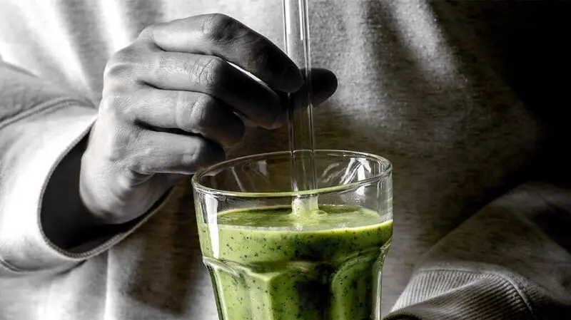 A person holding a glass straw getting ready to stir a green smoothie