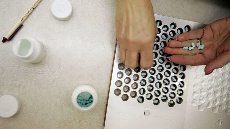 A person takes prescription pills out of bottles and organize them into a container on a table