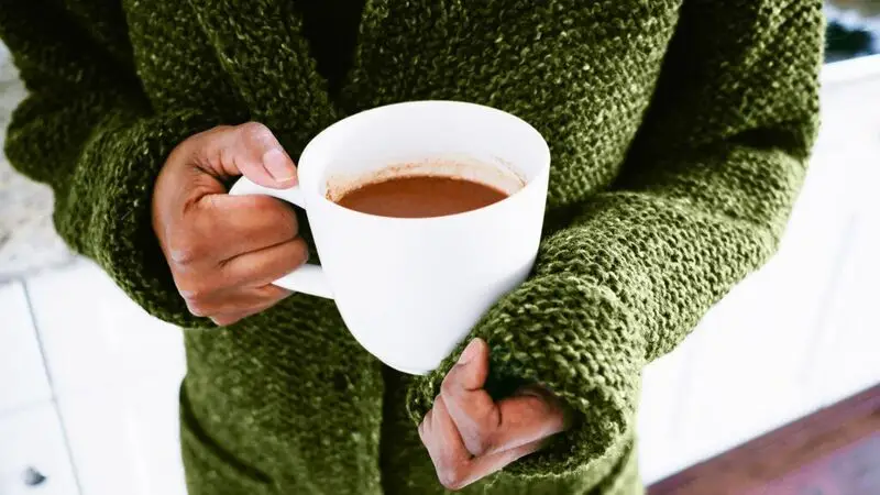 person in green jumper holding white mug of cocoa