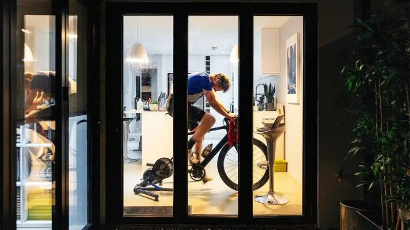 man exercising on stationary bike, seen through tall windows