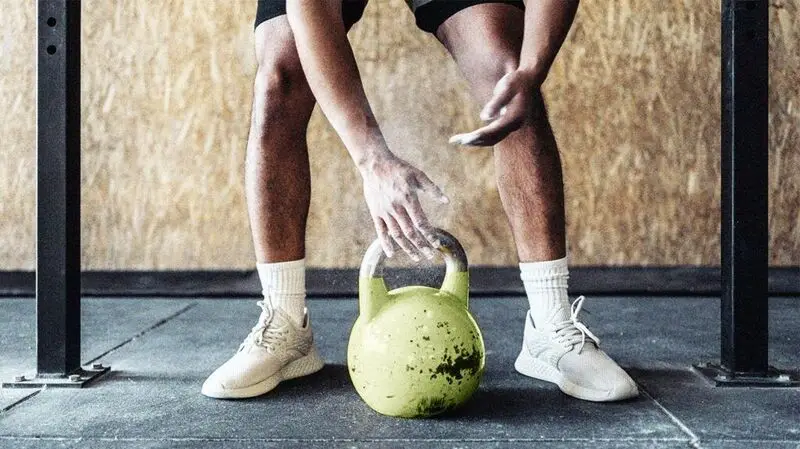 person's hands reaching for green-colored weight on gym floor