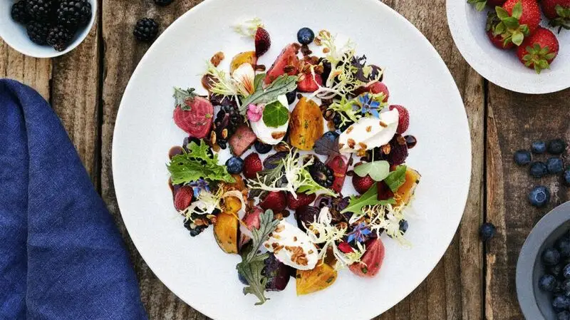 A plate of salad, consisting of roasted vegetables, fruits, and greens