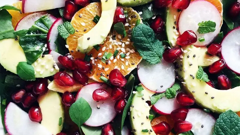 A colorful salad containing oranges, leafy greens, pomegranate, radishes, avocados, and seeds.