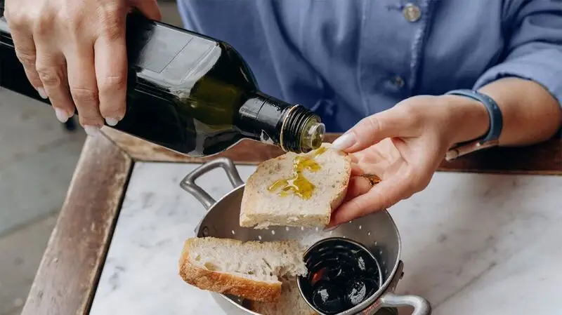 person's hands pouring olive oil over slice of bread