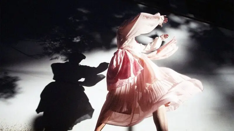 A woman dancing in a flowy dress as her shadow reflects on the floor