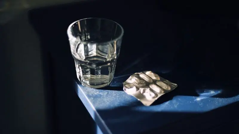 blister pack of pills next to a glass of water on a blue table