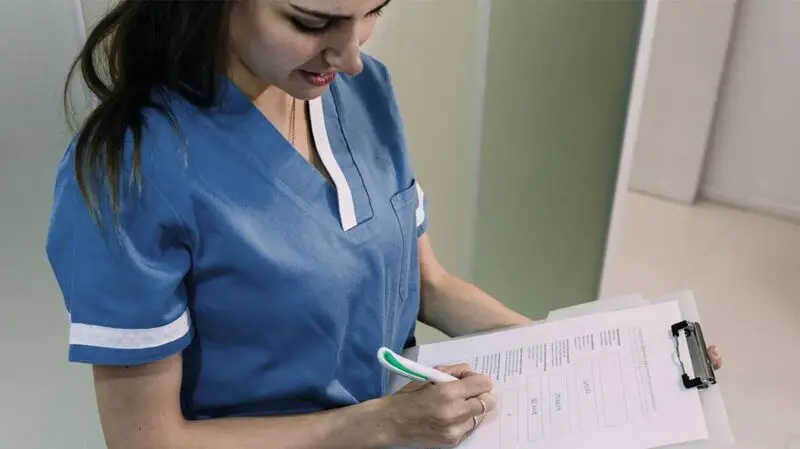 female doctor in blue scrubs checking notes