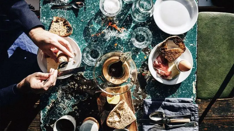 Aperson having breakfast with boiled eggs, sourdough bread, tea, and various other items early in the morning. 