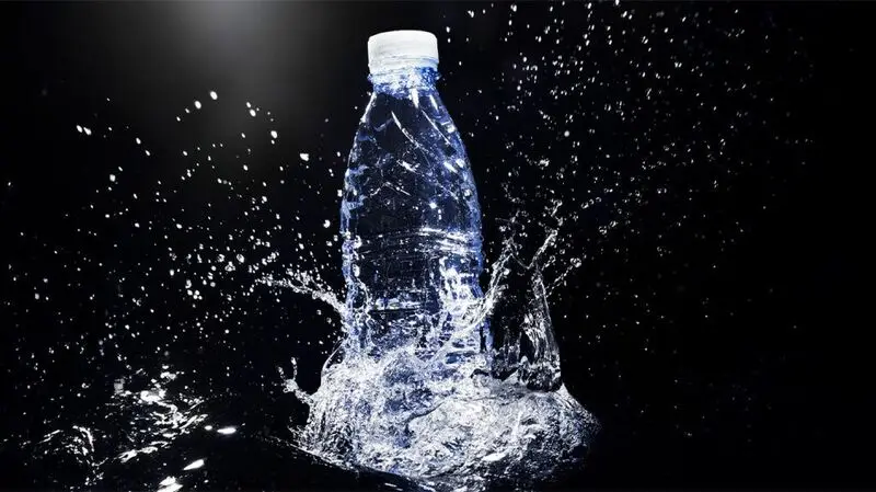 A bottle of carbonated sparkling water against a dark backdrop, falling onto a surface and splashing water around it