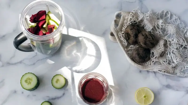 A nutribullet type blender full of cucumbers and beetroot for a juice cleanse on a flat surface