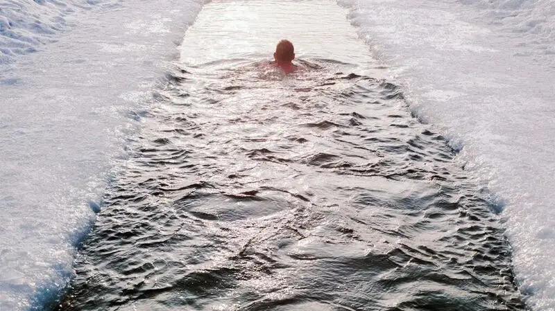 A person swims in a body of water surrounded by ice to emulate a cold plunge.