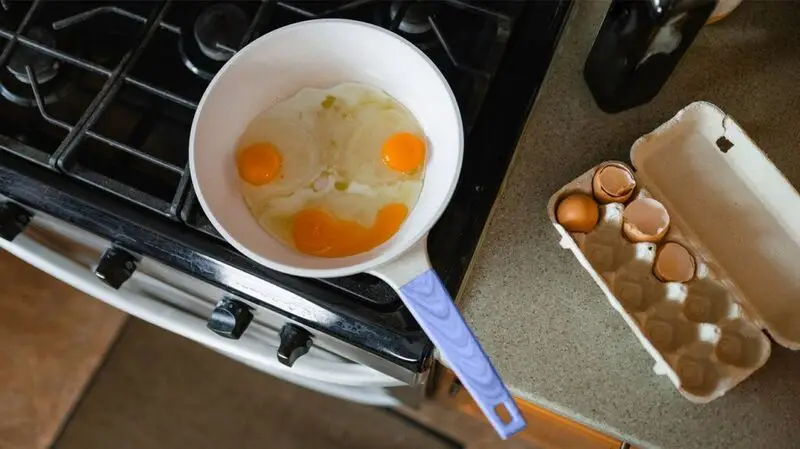 4 egggs in a pan create a smile with their yolks next to a box of cracked eggs