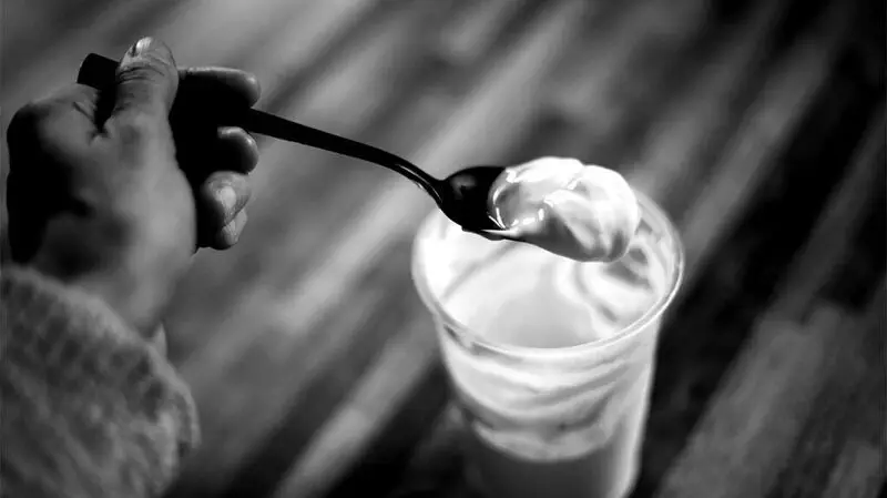 black and white photo of someone's hand lifting a spoonful of yogurt