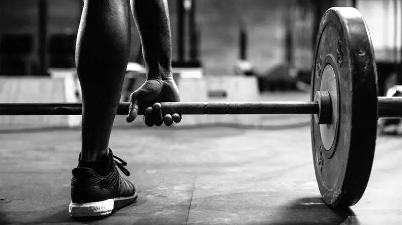 A close up of a person lifting a barbell loaded with weight at a gym