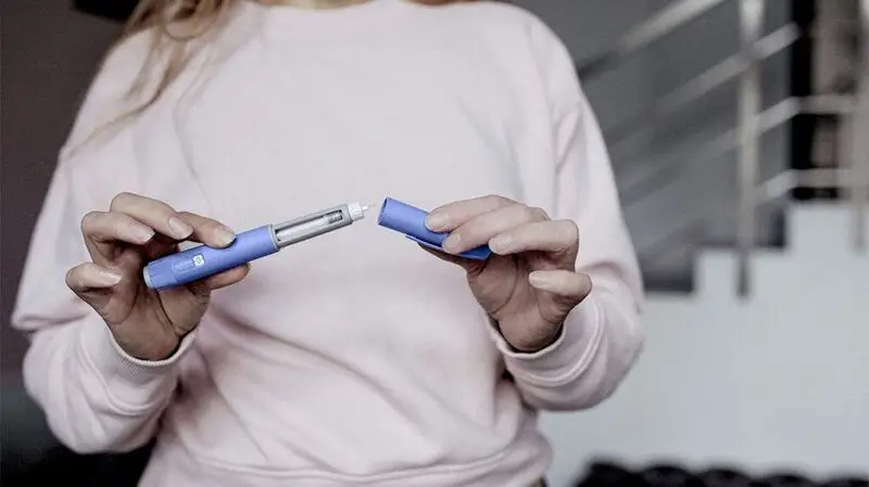 person in white sweater holding GLP-1 drug syringe