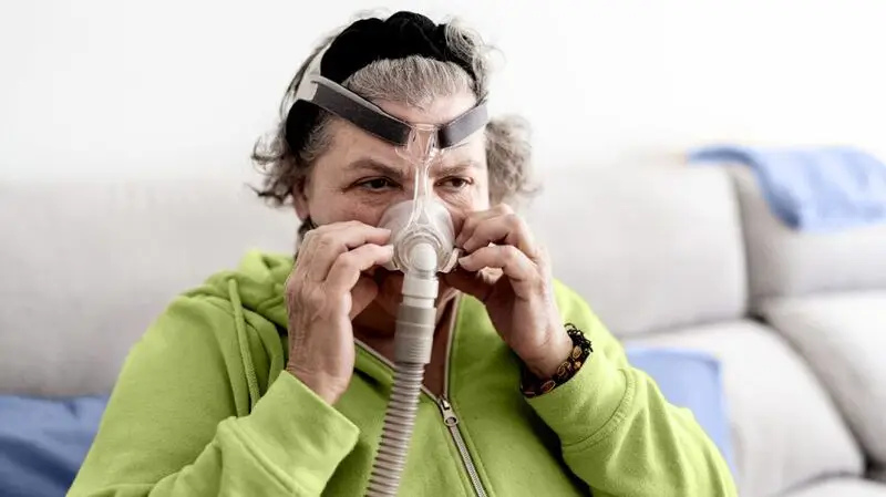 older white woman putting on the air flow mask of a CPAP machine