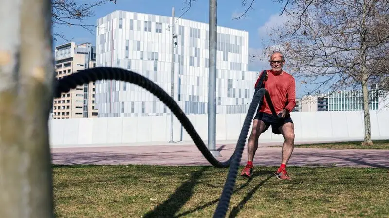 older white man doing battle rope exercise in a park