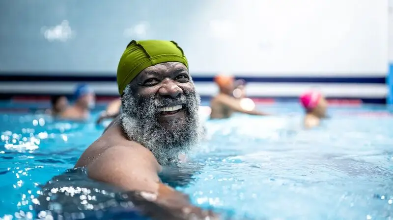 An older adult male swims in an indoor pool with a swimming cap