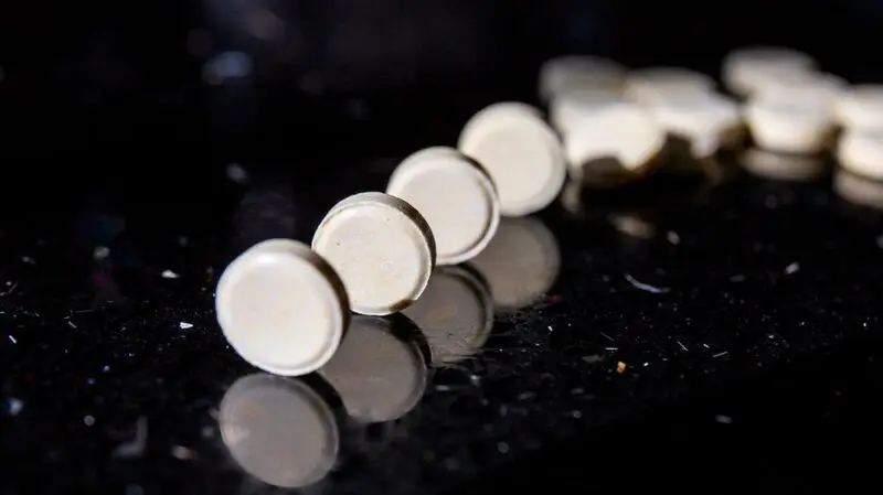 A row of vitamin A pills on a dark reflective surface