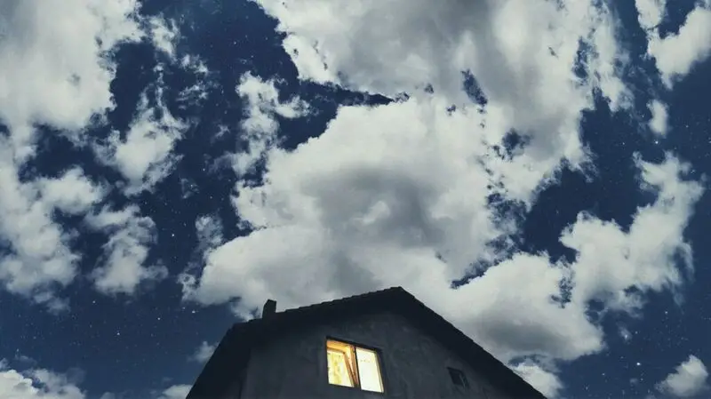 A lit up window in a house against a cloudy backdrop