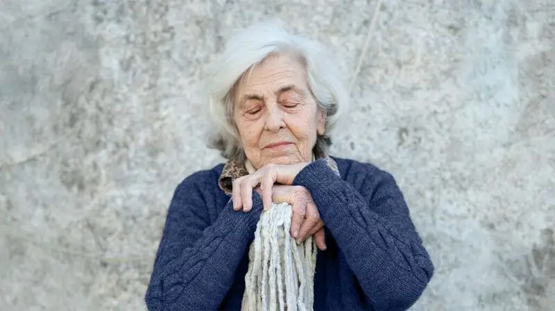 older white woman in blue cardigan with her eyes closed