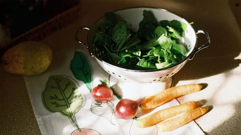 three carrots. two onions, and a bowl of spinach leaves on a table