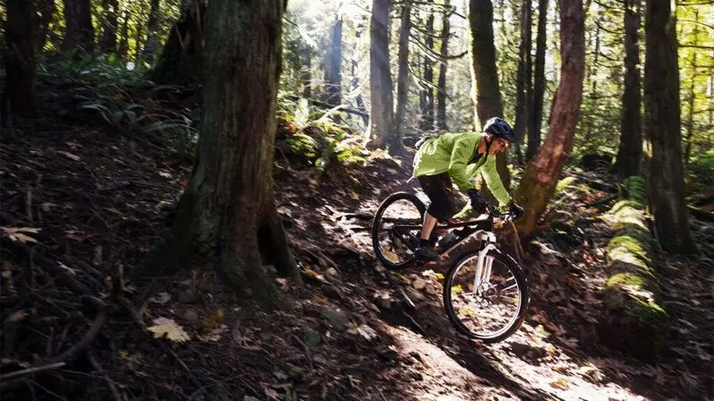 An older adult mountain biking in a forest, going down a hilly part