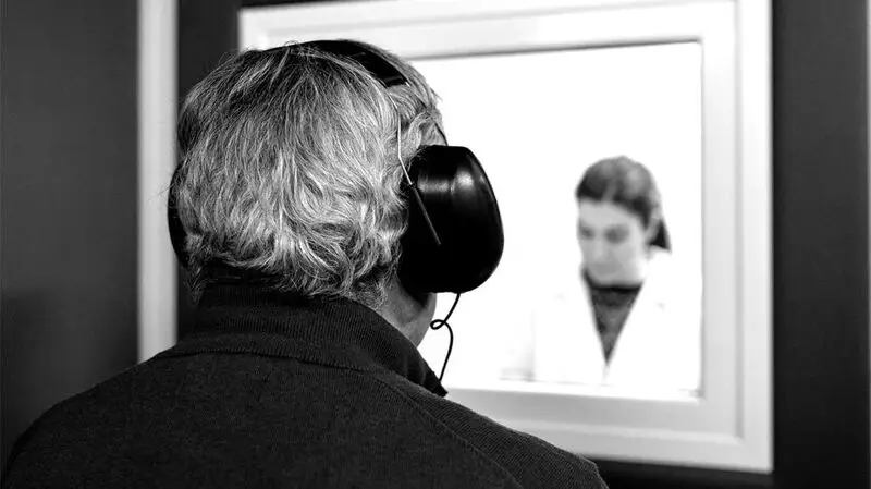 black and white photo of older man wearing headphones for hearing test in doctor's office
