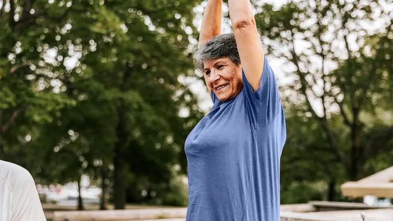 An older woman stretching her arms above her head outside