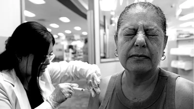 An odler adult woman gets vaccinated against shingles by a healthcare professional