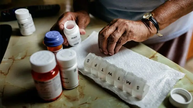 An older adult sorts out their medication into a seven-day pill box
