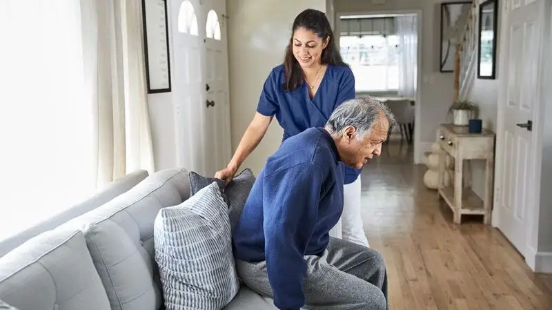 A nurse assists a senior adult sit down in a chair