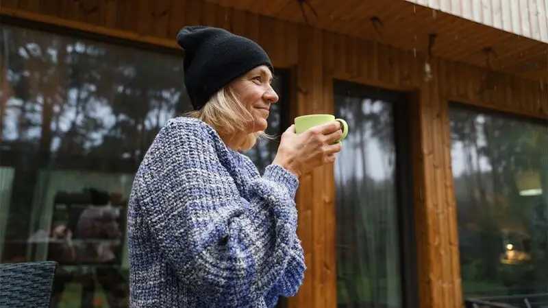mature white woman dressed in blue jumper and black beanie drinking from a green cup