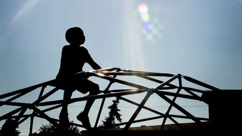 silhouette of child on playground climbing dome