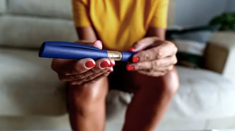 A woman sits on a sofa while holding a semaglutide injection, a GLP-1 agonst used to treat type 2 diabetes and aid weight loss