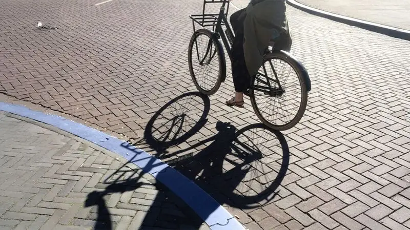 A person rides a bike as their shadow casts on the ground