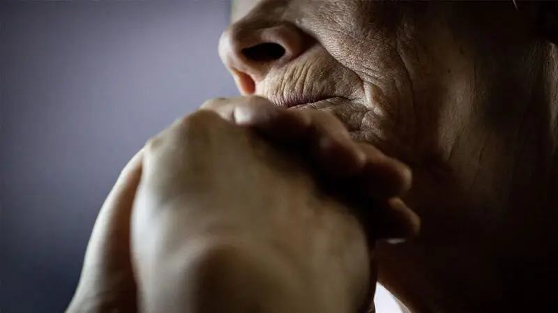 An older adult rests their chin on their hand