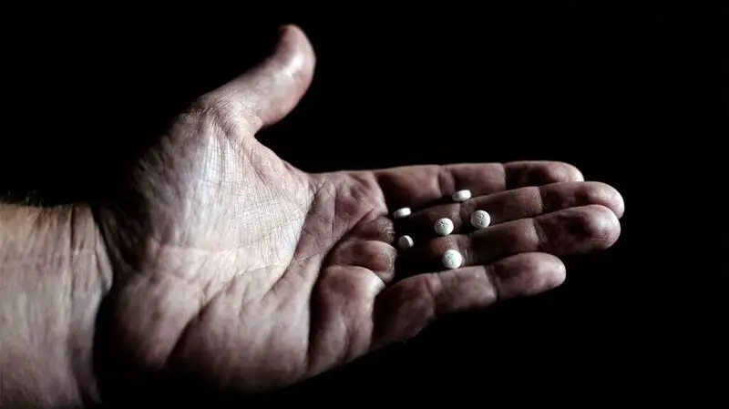 small white pills placed on person's hand shown against black background